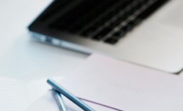 close-up photography of two pencils on closed pink covered book on desk near MacBook Air in a well-lit room