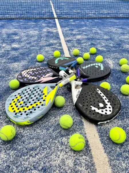 Four padel rackets arranged in a circle with yellow balls on a blue court